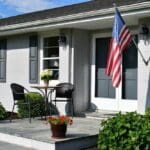 porch of a gray ranch painted brick house with an American flag