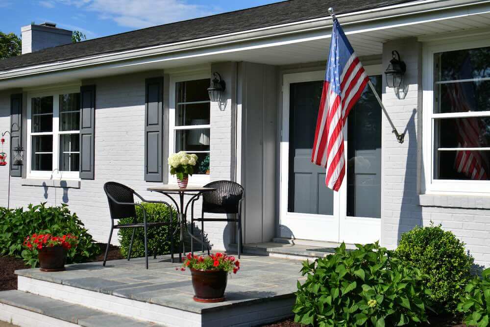 porch of a gray ranch painted brick house with an American flag
