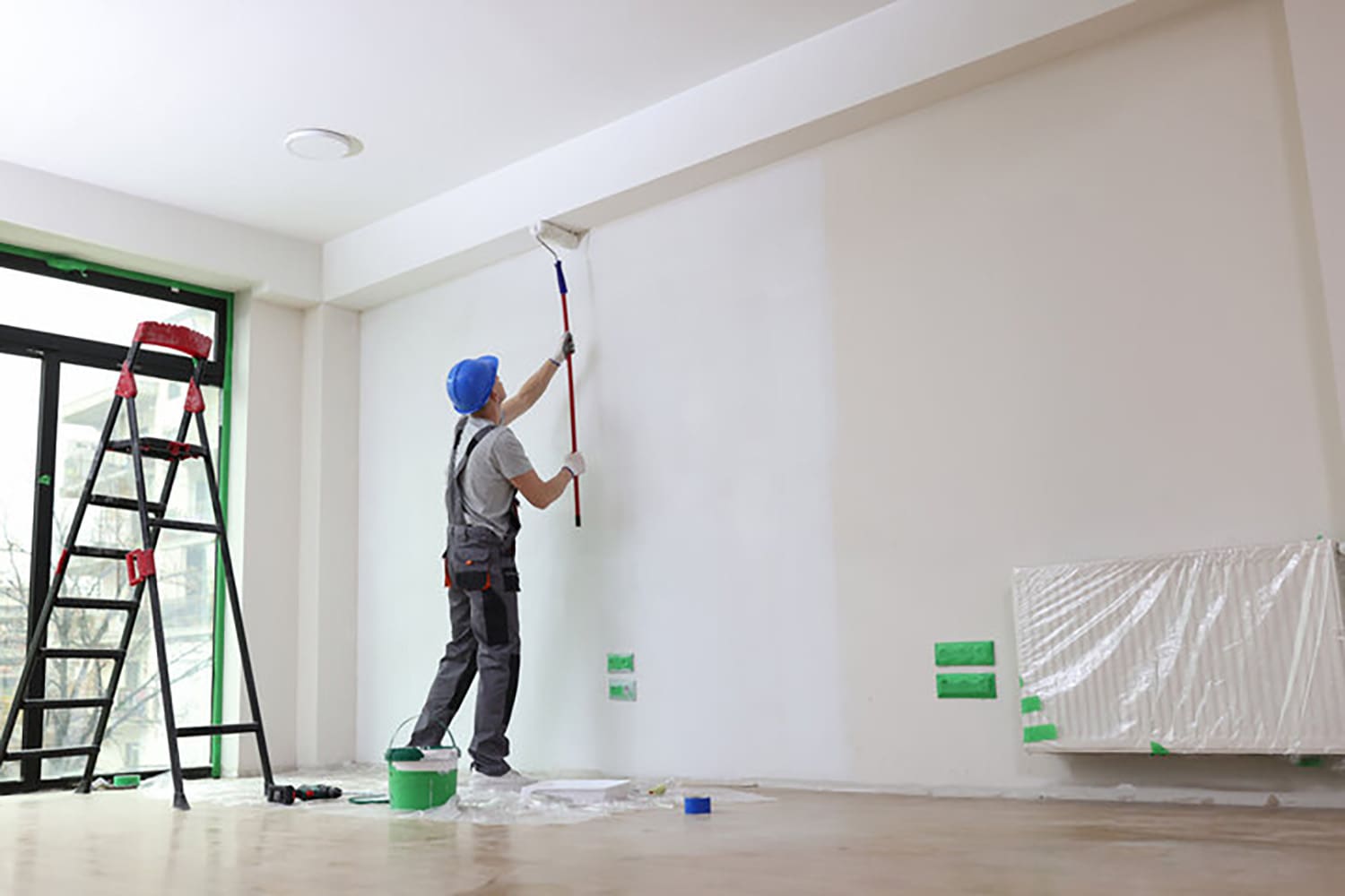 Interior painter applying fresh white paint to a living room wall, showing how long does interior paint last with proper preparation and technique