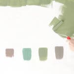 Hand applying paint samples on a wall to demonstrate how to choose paint colors for homes based on lighting and undertones