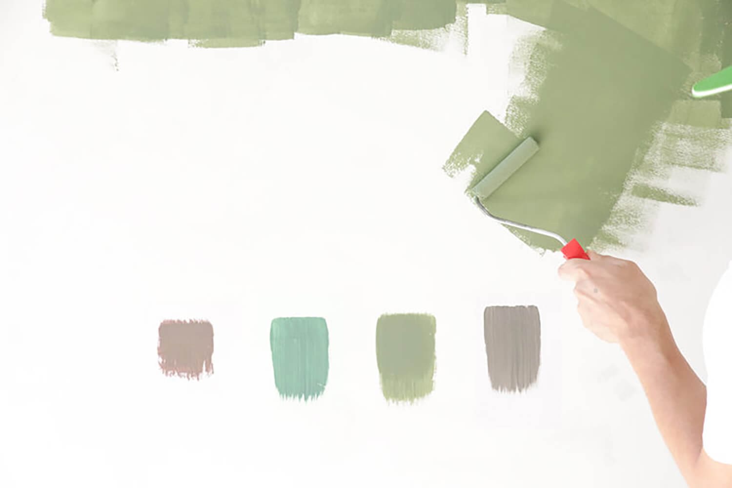 Hand applying paint samples on a wall to demonstrate how to choose paint colors for homes based on lighting and undertones