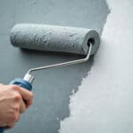 Interior paint colors that make rooms look larger applied with a roller, showing light gray paint creating a brighter, more open wall surface