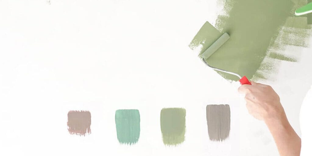 Hand applying paint samples on a wall to demonstrate how to choose paint colors for homes based on lighting and undertones