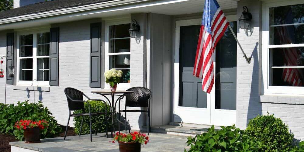 porch of a gray ranch painted brick house with an American flag